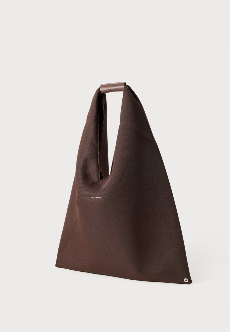 Brown fabric bag with an asymmetric shape, featuring a single strap and a subtle white stitching detail. Smooth texture with a clean design.