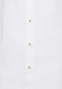 Vit skjorta i tyg med knappframsida och ljusa beige knappar, slät textur och avslappnad passform. Inga mönster eller detaljer.