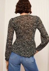 Musta-valkoinen kuviollinen peplum-toppi pitkähihaisilla hihoilla, jossa on röyhelöhelma ja teksturoitu kangas, yhdistettynä sinisiin farkk bottoms.
