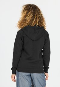 Haut à capuche noir avec une poche kangourou à l'avant et un cordon de serrage, fabriqué en tissu doux avec des poignets et un ourlet côtelés, porté sur un short en denim.