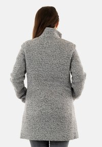 Manteau gris texturé avec un col haut et des manches longues, présentant une coupe droite et un design longueur genoux. Convient pour le temps frais.