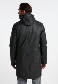 Lang zwarte regenjas van soepel, waterdicht materiaal, met een capuchon, verstelbare taille en subtiele stiksel-details.