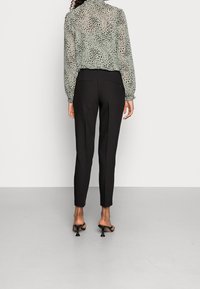 Przezroczysta zielona bluzka z czarnym nakrapianym wzorem, z marszczonymi rękawami; zestawiona z czarnymi dopasowanymi spodniami i czarnymi klapami na obcasie.