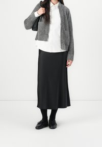 Šedý pletený cardigan s dvěma předními kapsami, bílá košile s knoflíky, černá saténová midi sukně, černé punčochové kalhoty a kožené mokasíny.