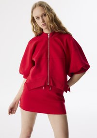 Rode oversized sweatshirt met rits, gemaakt van zacht materiaal, met korte pofmouwen en een asymmetrale zoom met trekkoordaccenten.