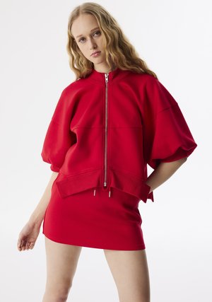 Rode oversized sweatshirt met rits, gemaakt van zacht materiaal, met korte pofmouwen en een asymmetrale zoom met trekkoordaccenten.