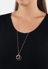 Roséguldhalsband med sammanflätade cirkulära hängen, prytt med ett delikat kedja, bärs över en svart tröja och framhäver dess eleganta design.