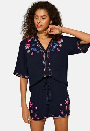 Marineblauer Jumpsuit mit kurzen Ärmeln, V-Ausschnitt und aufwendiger pinker und blauer Stickerei mit Blumen- und Meeresmotiven. Mit Taillenschnürung.