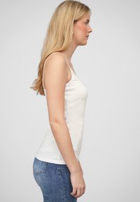 Haut sans manches blanc en tissu doux, au design ajusté, texture lisse, avec des bretelles étroites, présenté de côté.