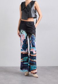 Veste courte en cuir noir avec un large col, associée à un pantalon large coloré à jambes larges présentant un motif mixte en bleu sarcelle, rose et bleu foncé.