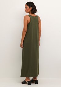 Rochie maxi fără mâneci, de culoare verde măsliniu, confecționată dintr-un material moale, având o croială lejeră și slituri laterale, purtată cu sandale negre cu toc bloc.