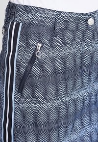 Szorty w granatowym wzorze z kropeczkami, z kieszenią na suwak z boku i jasnoniebieskimi paskami po bokach. Wykonane z lekkiej tkaniny.