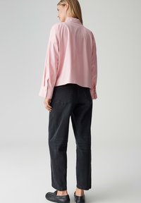 Light pink cropped shirt with a pointed collar and buttoned cuffs paired with high-waisted black jeans and black slip-on shoes.
