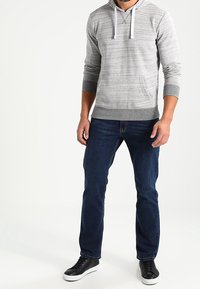 Sudadera con capucha de rayas grises con dobladillo gris, mangas largas, bolsillo delantero y cordones blancos, combinada con vaqueros azul oscuro y zapatillas negras.