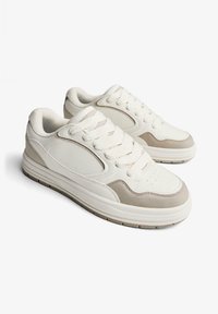 Bijele tenisice s bež detaljima, izrađene od kože i tkanine, s okruglim oblikom, debelim jastučićima na potplatu i dizajnom s vezicama.