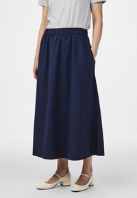 Tmavě modrá midi sukně s elastickým pasem, s bočními kapsami a hladkou texturovanou látkou. Doplněná krémově zbarvenými botami.