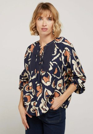 Blouse marine à motifs floraux en crème et rouille, avec un décolleté lacé, des manches élastiques et une coupe décontractée.