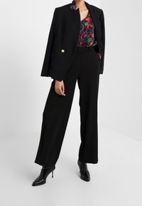 Blazer noir ajusté avec bouton doré, haut à motif floral, pantalons noirs taille haute et bottines noires à bout pointu.