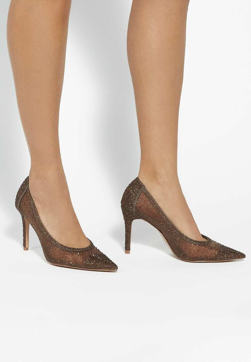 Brown stiletto heels made of mesh material, adorned with small metallic studs, featuring a pointed toe and slim high heel for an elegant silhouette.