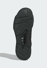 Semelle de sneaker noire avec des rainures texturées, des motifs angulaires et une section découpée transparente. Présente la marque 'TRAXION' sur le côté.