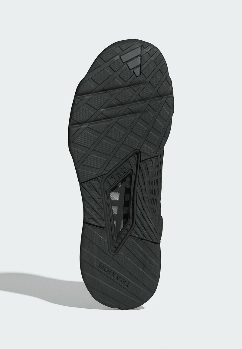 Sole di sneaker nera con scanalature testurizzate, modelli angolari e una sezione trasparente. Presenta il marchio 'TRAXION' sul lato.