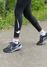 Leggings atletici neri con design a swoosh bianco, abbinati a scarpe da corsa grigie e calzini bianchi alla caviglia con un piccolo logo.
