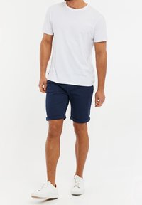 Camiseta blanca de cuello redondo, pantalones cortos navy enrollados y zapatillas blancas. Atuendo casual con un diseño sencillo y colores contrastantes.