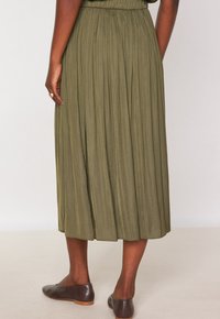 Gonna midi plissettata verde oliva con cintura elastica, realizzata in materiale leggero, abbinata a scarpe basse marroni.