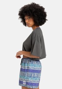 Grå cropped t-skjorte med løse ermer, paret med flerfargede mønstrede shorts som har blå, lilla og hvite geometriske design.