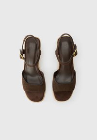 Pair of dark brown suede open-toe sandals with ankle straps and gold buckles, flat soles, and cushioned insoles on a white background.