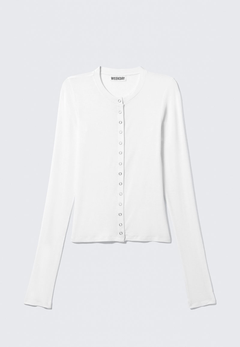 Cardigan bianco a maniche lunghe in tessuto morbido con scollo tondo e sette bottoni lungo la parte anteriore. Design semplice e aderente.