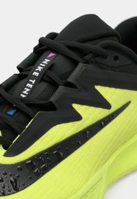 Παπούτσι τένις Nike με φωτεινό νέον κίτρινο επάνω μέρος, μαύρες συνθετικές επιστρώσεις, υφή υφάσματος και ξεχωριστό μαύρο Swoosh με σταγόνες νερού.