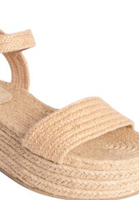 Sandalia de esparto trenzada en color beige con una gruesa plataforma, que cuenta con dos cintas anchas y un tacón curvado. La tela texturizada complementa las fibras naturales.