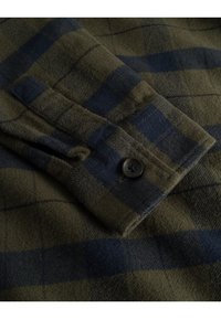 Groen en marineblauwe geruite flanellen shirt met een mouw met een knoopmanchet; zachte textuur met zichtbare stofweef en contrasterend geruit patroon.