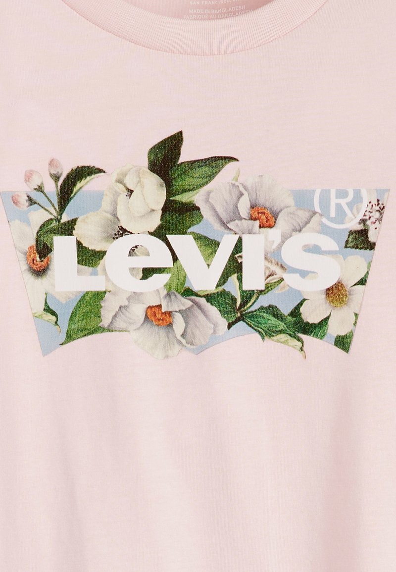 Jasnoróżowa koszulka z dużą kwiatową grafiką, na której znajdują się białe kwiaty i zielone liście, na niebieskim tle, z napisem "Levi's" w wyraźnej białej czcionce.