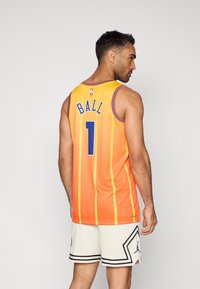 Oranžový basketbalový dres s vertikálnymi pruhmi, s nápisom "BALL" a číslom "1" v modrej farbe. Nosí sa s bielymi perforovanými šortkami a čiernymi akcentmi.