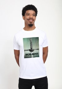 Hvid bomuld t-shirt med et grafisk design af et sværd med udsmykkede detaljer og teksten "HIGHLANDER" i fed grøn skrift.