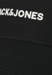 Black cap made of textured fabric, featuring a white logo "BACK&JONES" on the front. Visor is flat with subtle stitching detail.
