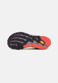 Suela de zapato de trail running con tacos agresivos en naranja y púrpura, con una entresuela gris y un logo de Vibram cerca del talón.