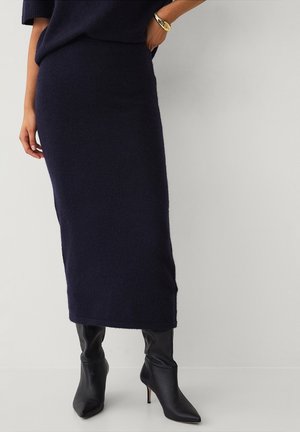 Navy knitted midi skirt with a fitted waist and straight silhouette. Paired with sleek black heeled boots and a bracelet on the wrist.