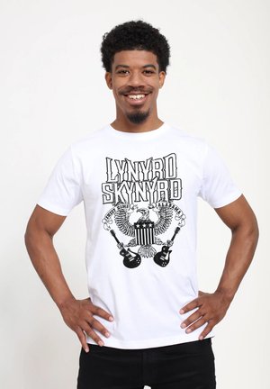 Hvid bomulds T-shirt med sort grafisk design af "Lynyrd Skynyrd," ørne, stjerner og guitarer. Korte ærmer, rund hals.