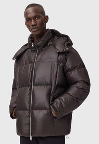 Mørkebrune pufferjakke med lynlås foran, oversized krave, quiltet design og sidelommer. Lavet af skinnede, glatte materialer.