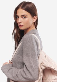 Szary sweter dzianinowy z ściągaczami w mankietach, z kołnierzykiem; modelka niesie jasnobeżową torbę pikowaną z paskami na ramię.