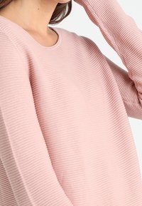 Light pink sweater with a round neckline, ribbed texture, and long sleeves. Fabric appears soft and slightly stretchy.