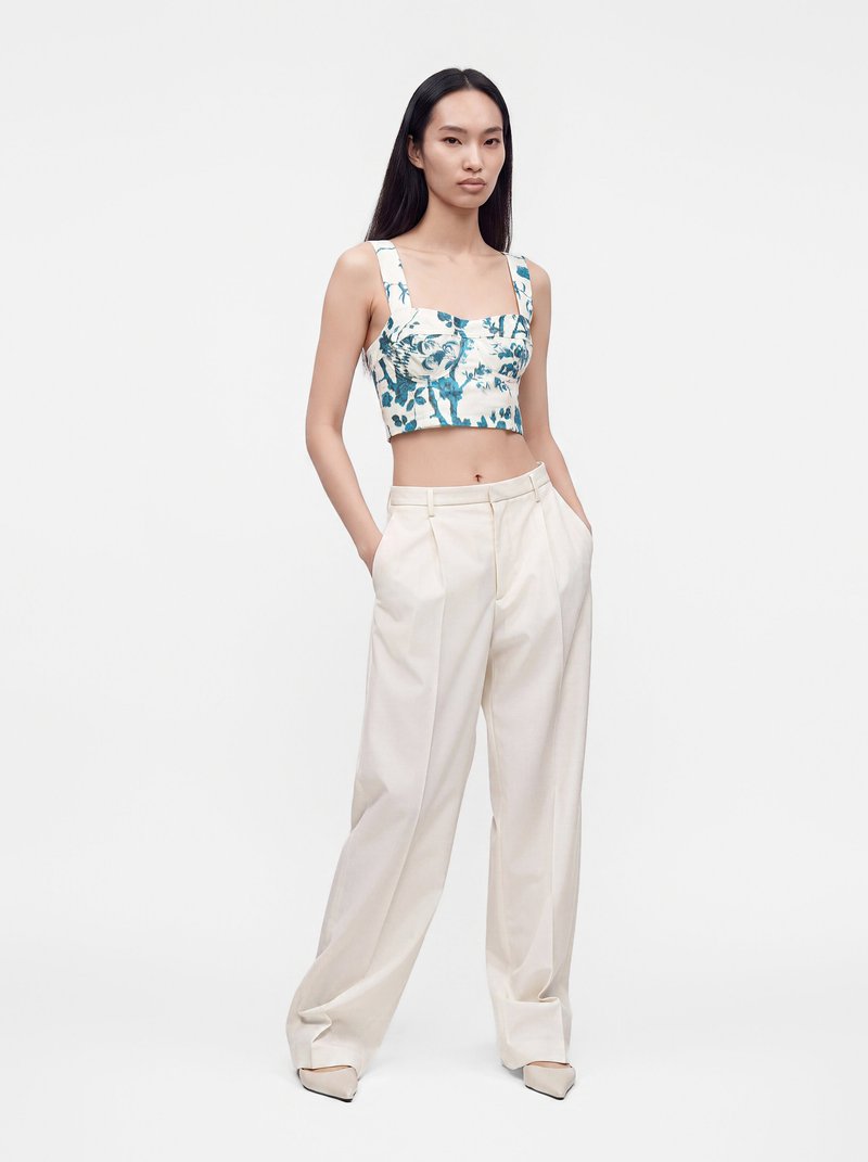 Femme portant un crop top à fleurs bleu et blanc associé à un pantalon crème taille haute à jambes larges et des chaussures pointues crème.