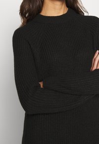 Schwarzer Strickpullover mit ribbeliger Textur, Rundhalsausschnitt und langen Ärmeln. Das Design zeichnet sich durch eine lockere Passform und Raglanärmel aus.