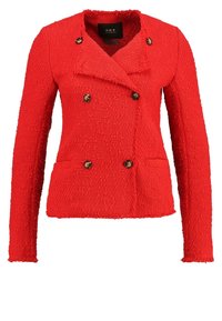 Veste double boutonnage rouge texturée avec des manches longues, deux poches avant et boutons ronds marron. Elle présente un col cranté et une longueur courte.