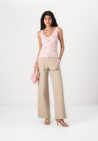 Top in cotone a coste rosa pallido con ricami floreali, abbinato a pantaloni beige a gamba larga e una pochette rosa. Tacchi beige con cinturini completano il look.