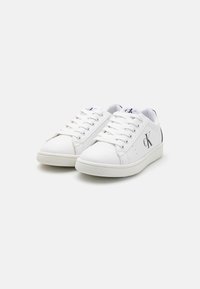 Baskets en cuir blanc avec six œillets, lacets plats, logo sur le côté et semelles en caoutchouc texturé. Bout arrondi et accents de talon contrastés.