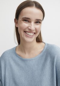 Lyseblå, blød striktrøje med bredt rundt halsudskæring og afslappet pasform. Subtil tekstur synlig i stoffet.
